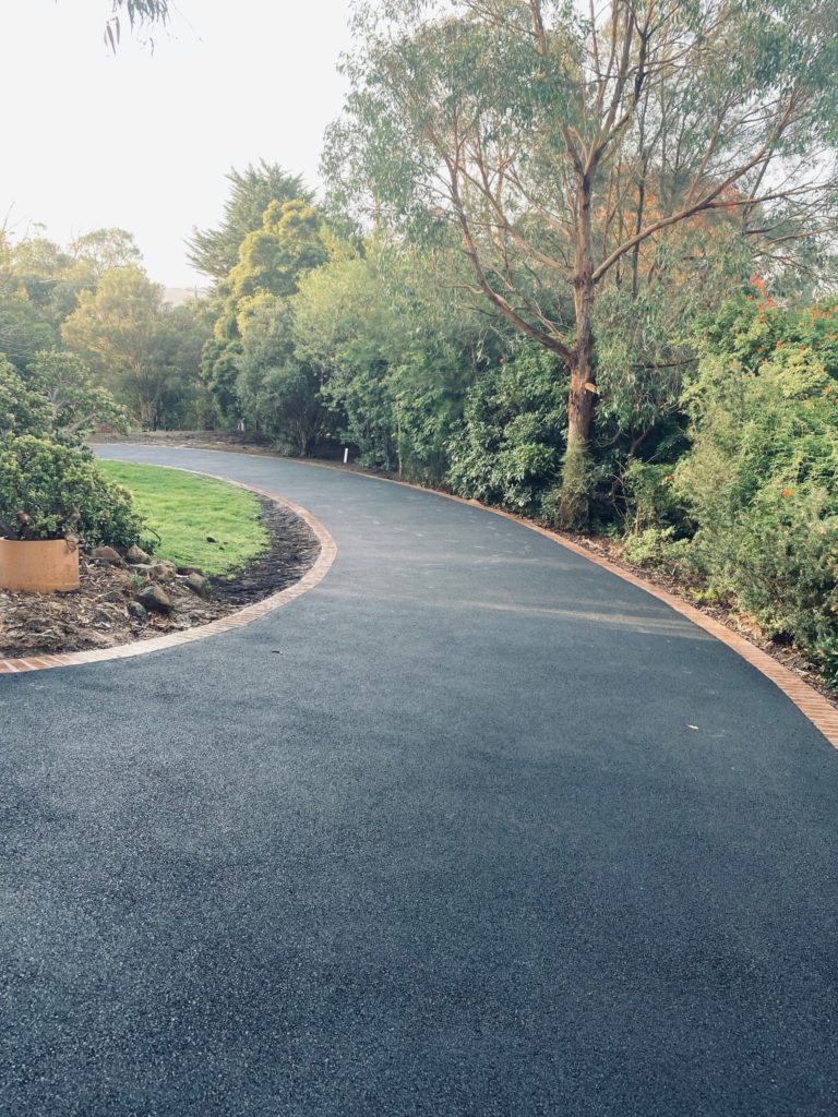 An evenly curved brick edged asphalt driveway with a native garden in Belgrave South