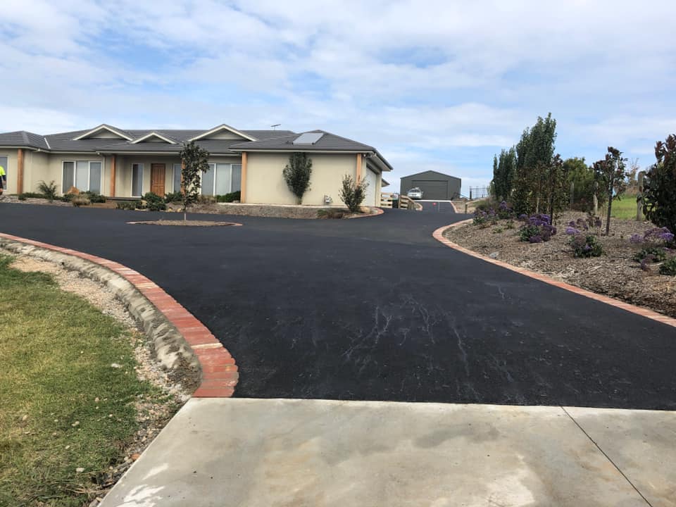 looking up a large asphalt turning area to a house, a small tree in the turning circle